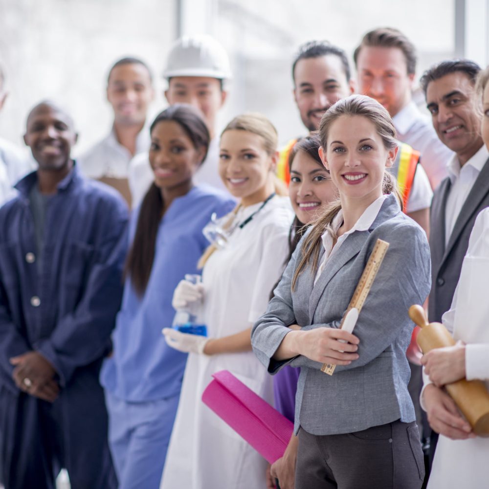 A multi-ethnic group of varied business professionals are standing together and are smiling while looking at the camera.